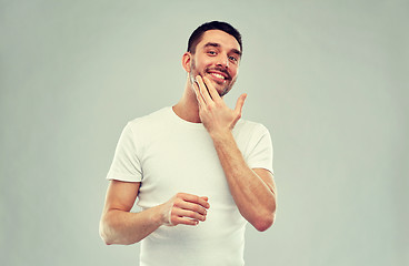 Image showing happy young man applying cream or lotion to face