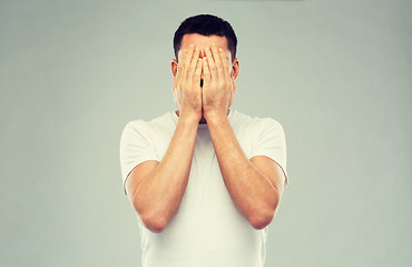 Image showing man in white t-shirt covering his face with hands