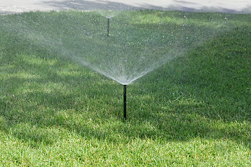 Image showing Sprinkler spraying stream of water on lush green grass