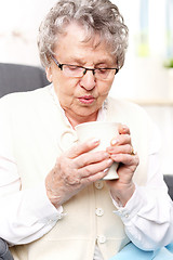 Image showing Grandma's first aid kit, an infusion of herbs. Mature woman resting on a chair with a cup of brew with herbs