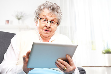 Image showing Surprised elderly woman looks in the tablet screen