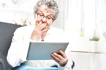 Image showing University of the Third Age. Surprised elderly woman looks in the tablet screen Elderly woman surfs the internet.