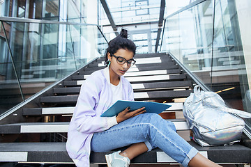 Image showing young cute indian girl at university building sitting on stairs reading a book, wearing hipster glasses, lifestyle people concept