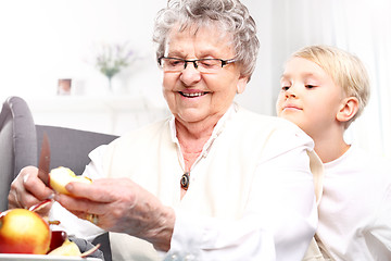 Image showing Grandmother looks after the child. Grandmother to grandchild picks an apple peel