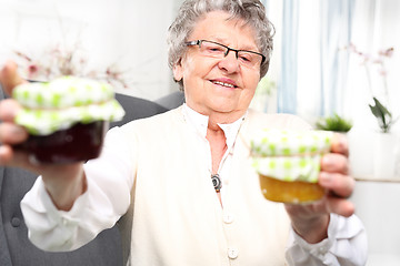 Image showing A gift from her grandmother, colorful jam. Mature woman with personally prepared jars of jams. 