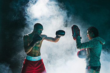 Image showing Handsome Afro American boxer with bare torso is practicing punches with a partner at the fight club