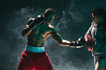 Image showing Handsome Afro American boxer with bare torso is practicing punches with a partner at the fight club