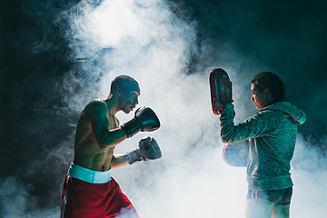 Image showing Handsome Afro American boxer with bare torso is practicing punches with a partner at the fight club