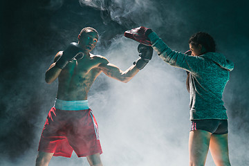 Image showing Handsome Afro American boxer with bare torso is practicing punches with a partner at the fight club