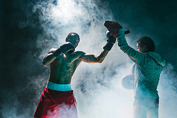 Image showing Handsome Afro American boxer with bare torso is practicing punches with a partner at the fight club