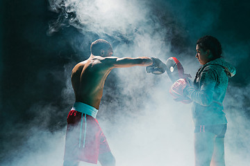 Image showing Handsome Afro American boxer with bare torso is practicing punches with a partner at the fight club