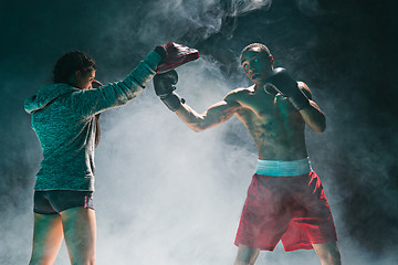 Image showing Handsome Afro American boxer with bare torso is practicing punches with a partner at the fight club