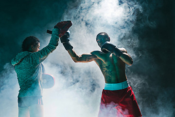 Image showing Handsome Afro American boxer with bare torso is practicing punches with a partner at the fight club