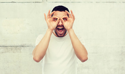 Image showing man making finger glasses over gray background