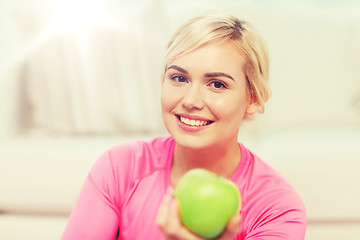 Image showing happy woman eating green apple at home