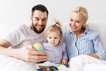 Image showing happy family with smartphone in bed at home