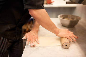 Image showing chef with rolling-pin rolling dough at kitchen