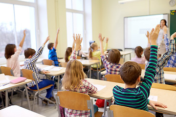 Image showing group of school kids raising hands in classroom