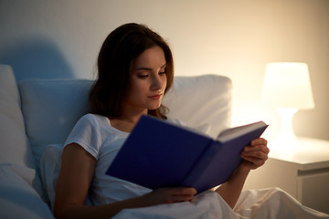 Image showing young woman reading book in bed at night home