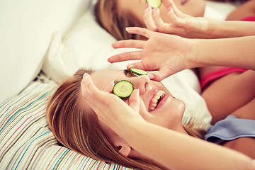 Image showing happy young women with cucumber mask lying in bed