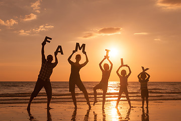 Image showing Happy family standing on the beach at the sunset time.