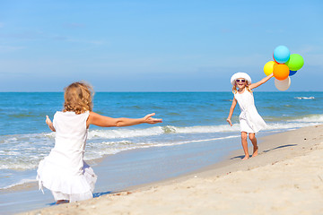 Image showing Mother and daughter playing with balloons on the beach at the da