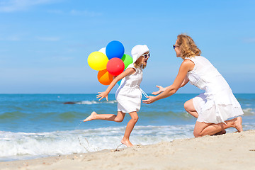 Image showing Mother and daughter playing with balloons on the beach at the da