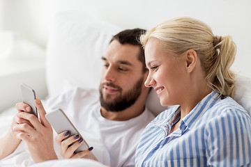 Image showing happy couple with smartphones in bed at home
