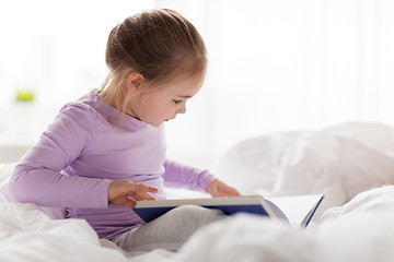 Image showing happy little girl reading book in bed at home