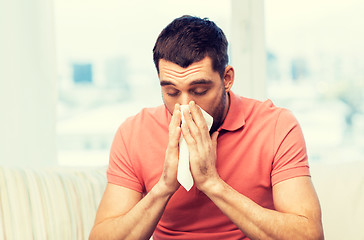 Image showing sick man blowing nose to paper napkin at home