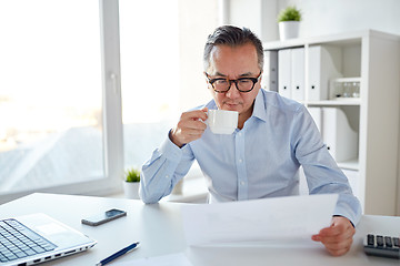 Image showing businessman with papers drinking coffee at office