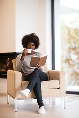 Image showing black woman reading book  in front of fireplace