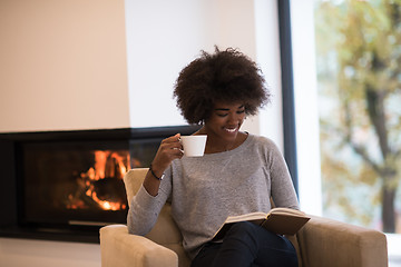 Image showing black woman reading book  in front of fireplace