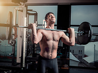 Image showing Portrait of super fit muscular young man working out in gym with barbell