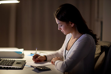 Image showing woman with calculator and papers at night office