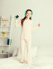 Image showing girl jumping on bed with smartphone and headphones