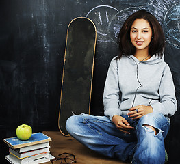 Image showing young cute teenage girl in classroom at blackboard seating on ta