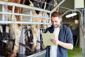 Image showing man with clipboard and milking cows on dairy farm