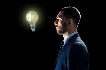 Image showing businessman looking at lightbulb over black