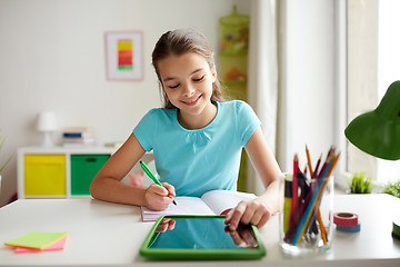 Image showing girl with tablet pc writing to notebook at home