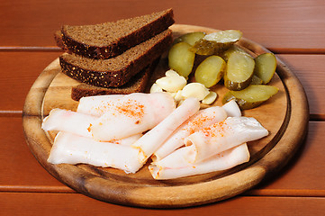 Image showing Wooden plate with smoked bacon, pickles and rye bread