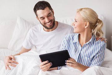 Image showing smiling happy couple with tablet pc in bed at home