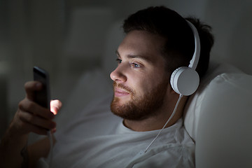 Image showing man with smartphone and headphones in bed at night