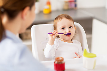 Image showing baby girl with spoon eating puree from jar at home