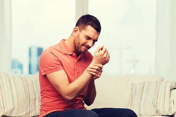 Image showing unhappy man suffering from pain in hand at home