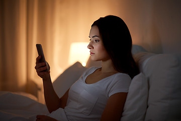 Image showing young woman with smartphone in bed at night