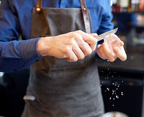 Image showing bartender grinding ice cube with knife at bar