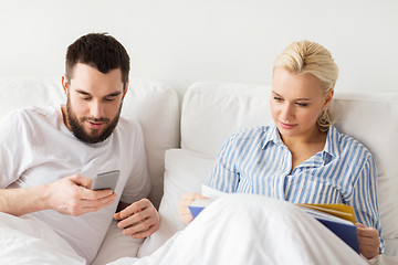 Image showing couple with book and smartphones in bed at home