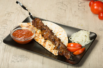 Image showing shashlik. kebab skewer, black rectangular plate. sauce and onions