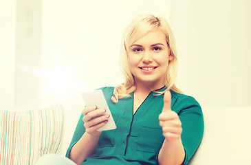 Image showing woman with smartphone showing thumbs up at home